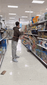 a man in a brown hoodie is standing in a store aisle holding a hula hoop
