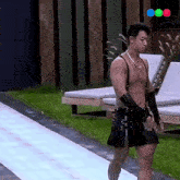 a shirtless man wearing suspenders and a skirt walks down a path