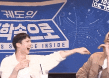 a man laughs in front of a blue sign that says science inside