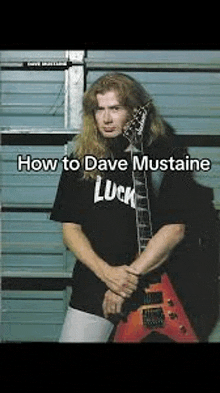 a man with long hair is holding a guitar and wearing a black shirt that says luck .