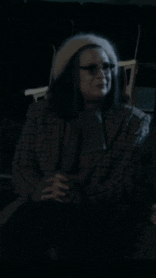a woman wearing a hat and glasses is sitting in a dark room .