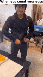 a man in a black jacket is standing in front of a table with a notebook on it .