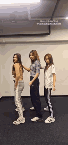 three women are standing next to each other in a room and one of them is wearing a white shirt