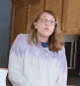 a young girl wearing glasses and a purple tie dye sweatshirt is standing in a kitchen .