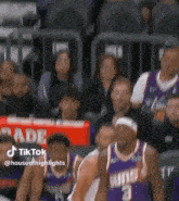 a group of basketball players in purple uniforms are standing in front of a crowd .