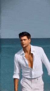 a man in a white shirt and white pants is standing on a beach .