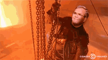a cartoon of a man hanging from chains with comedy central written on the bottom right
