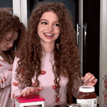 a woman with curly hair is smiling while holding a bottle of nutella
