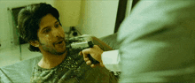 a man is laying on a bed while a man holds a gun to his face
