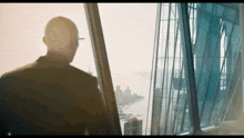 a man in a suit is standing in front of a tall building looking out a window .