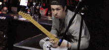 a man playing an electric guitar in front of a bar with a man in a staff shirt behind him
