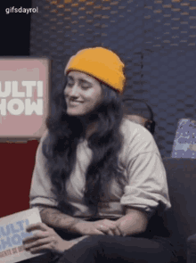 a woman wearing a yellow beanie is sitting in front of a sign that says multi show .