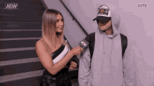 a woman is talking to a man with a microphone while standing next to a staircase .