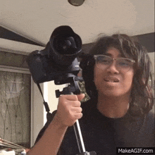 a young man with long hair is holding a camera on a tripod .