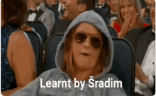 a woman wearing a hoodie and sunglasses is sitting in a crowd of people and says learnt by sradim .