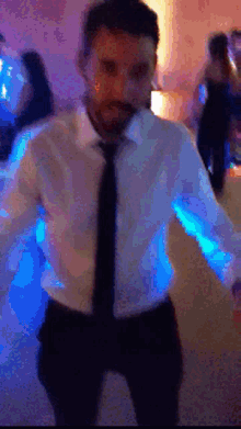 a man in a white shirt and tie is dancing in a dark room