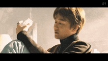a man in a turtleneck is holding a piece of paper with the letter s on the bottom