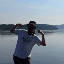 a man flexes his muscles in front of a body of water wearing a t-shirt that says tough xtreme