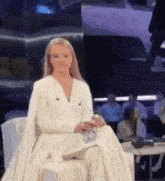 a woman in a white dress is sitting in front of a crowd