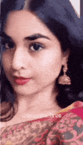 a close up of a woman 's face wearing a pink saree and earrings .