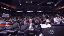 a man in a suit sits in the stands at a basketball game