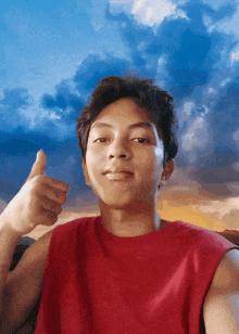 a young man in a red shirt is giving a thumbs up sign