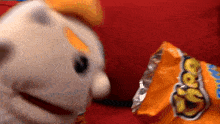 a puppet is eating a bag of cheetos on a red couch