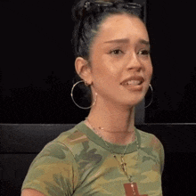 the woman is wearing a camouflage shirt and hoop earrings .