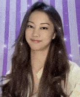 a woman with long hair is smiling in front of a purple striped wall .