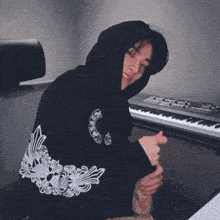 a man in a black hoodie is sitting in front of a piano keyboard