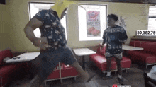 a man wearing a banana hat is dancing in a diner with another man .