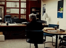 a man sits at a desk in an office with a poster on the wall that says ' united states ' on it