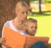 a woman is reading a book to a little girl while sitting under a tree ..