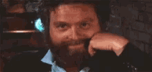 a man with a beard is smiling and touching his face .