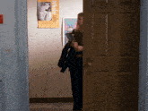 a woman standing in front of a door with a poster on the wall that says " guess who 's coming out "