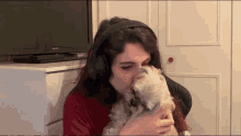 a woman wearing headphones kisses a small white dog in front of a sony television