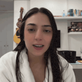 a woman in a white robe stands in front of a guitar and a shelf with pop figures on it