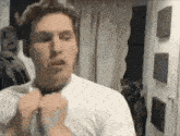 a man in a white shirt is adjusting his tie in a living room .