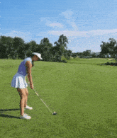 a woman in a purple shirt and white skirt is swinging a golf club