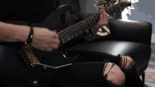 a man is playing a guitar in a chair with ripped jeans
