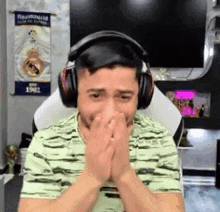 a man wearing headphones is covering his mouth with his hands while sitting in front of a tv .