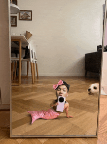 a baby dressed as a mermaid is taking a selfie in a mirror