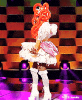 a woman in a pink and white dress is dancing on a stage in front of purple lights .