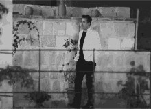 a man in a white jacket is standing in front of a brick wall .