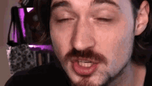 a man with a beard is making a funny face with his eyes closed and his mouth open .