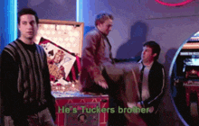 three men are standing in front of a pinball machine that says he 's tuckers brother