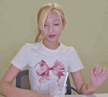 a woman in a white shirt with a pink bow on it is clapping