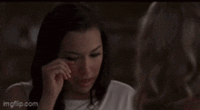 two women are standing next to each other in a dark room . one of the women is wearing a white shirt .