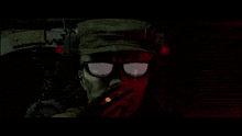 a man wearing glasses and a hat is smoking a cigarette in the dark