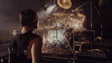 a man stands in front of a drum set with the letter d in the corner